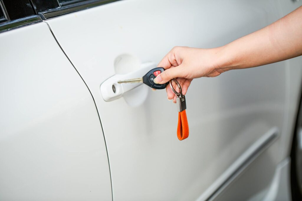 Close-up of a hand unlocking a white car door with a metal key and key fob.